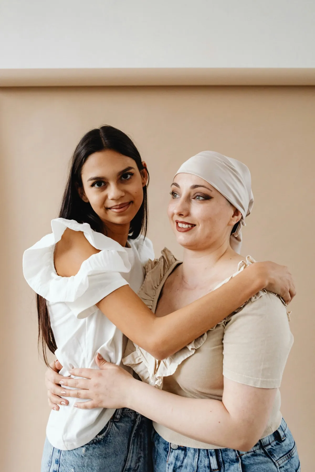 A woman wearing a head scarf embracing a younger woman, both smiling
